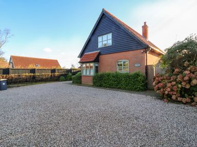 A gravel driveway in front of a house with a tiled roof and a black wooden upper facade at Mellows Thorpeness