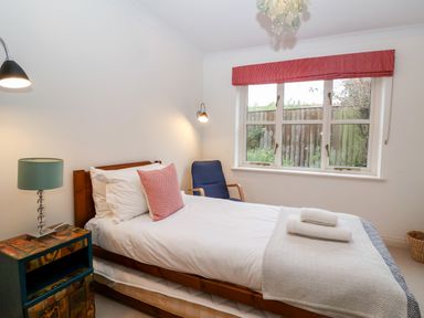 A bedroom with a single bed bedside table with a lamp blue armchair and window with red blind at Mellows Thorpeness in Thorpeness