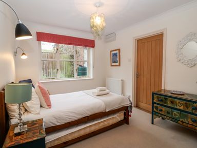 A bedroom with a single bed with white linens a bedside table with a lamp a window with a red blind a wooden door a dresser with hearts painted on it and a mirror on the wall at Mellows Thorpeness in Thorpeness