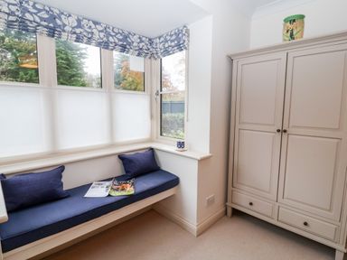 A window seat with blue cushions and magazines beside a cream wardrobe topped with a vase at Mellows Thorpeness