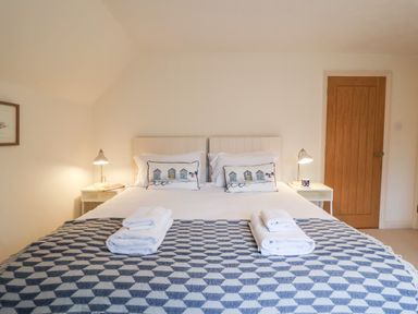 A bedroom with a double bed two bedside tables with lamps towels on the bed and a wooden door at Mellows Thorpeness in Thorpeness