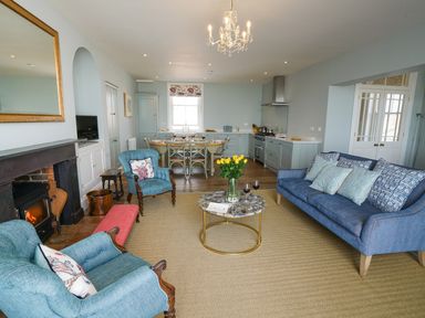 An open plan living room and kitchen with blue sofas wooden dining table and a fireplace at Shingle Skies Aldeburgh