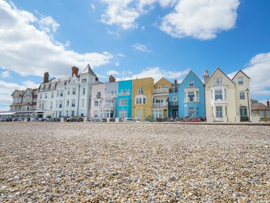 A row of colorful houses along a pebble beach under a partly cloudy sky at Shingle Skies Aldeburgh