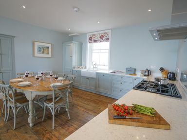 A kitchen with a wooden dining table set for six people and a countertop with vegetables and cooking utensils at Shingle Skies Aldeburgh