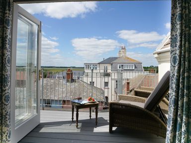 A balcony with two wicker chairs and a small table holding strawberries sunglasses and a magazine overlooking rooftops at Shingle Skies Aldeburgh