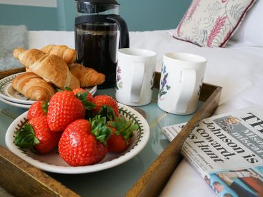 A tray with croissants strawberries a coffee pot two mugs and a newspaper on a bed at Shingle Skies Aldeburgh