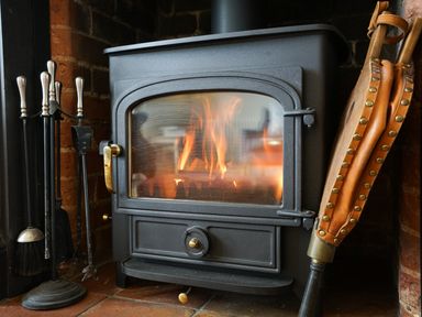 A wood burning stove with fire inside and fireplace tools at Shingle Skies Aldeburgh