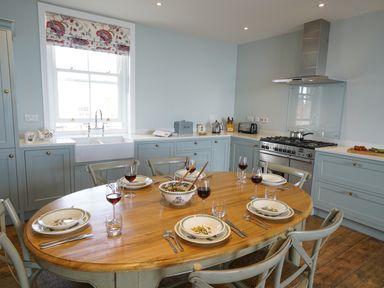 A kitchen with a wooden dining table set for six with plates and wine glasses at Shingle Skies Aldeburgh