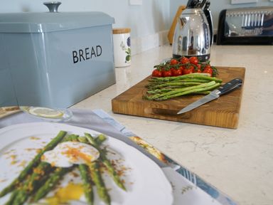 A kitchen countertop with a bread box asparagus and tomatoes on a cutting board a knife a kettle and a toaster at Shingle Skies Aldeburgh