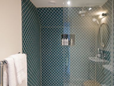 A shower with patterned blue and white tiles towels on a rack at Shingle Skies Aldeburgh