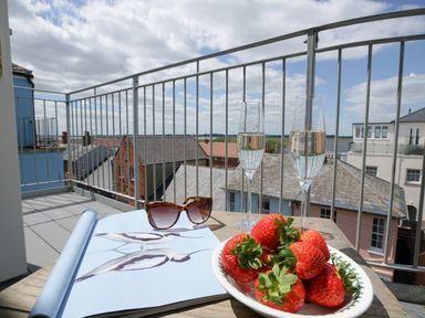 A balcony with two glasses of sparkling wine a bowl of strawberries sunglasses and a book showing bird illustrations at Shingle Skies Aldeburgh