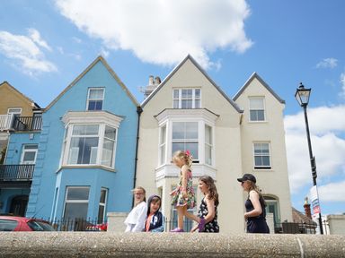 Children walking on a stone wall in front of two houses with triangular roofs at Shingle Skies Aldeburgh in Aldeburgh