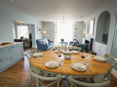A dining table set with plates and glasses in a living room with sofas and a fireplace at Shingle Skies Aldeburgh in Aldeburgh