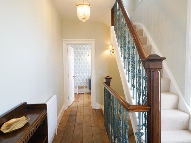 A hallway with wooden floor and staircase with blue railing leading upstairs at Shingle Skies Aldeburgh