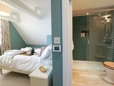A bedroom with a bed and breakfast tray next to a bathroom with a glass shower at Shingle Skies Aldeburgh in Aldeburgh