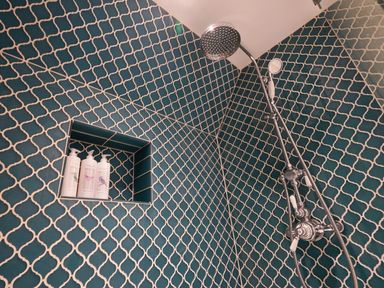 A shower area with blue patterned wall tiles and chrome shower fixtures at Shingle Skies Aldeburgh