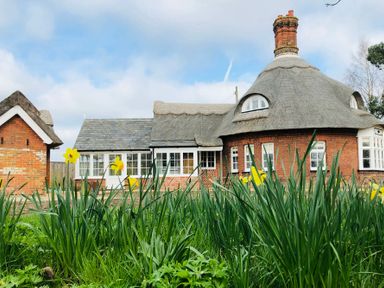 A brick house with a thatched roof and yellow flowers in the foreground at The Round House in Easton near Framlingham