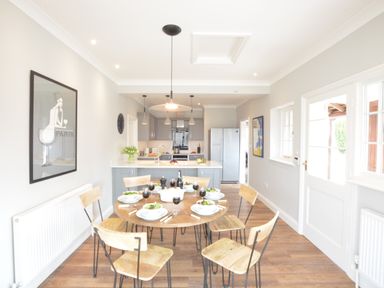 A dining area with a round wooden table set for six meals next to a kitchen with gray cabinets at The Round House in Easton near Framlingham