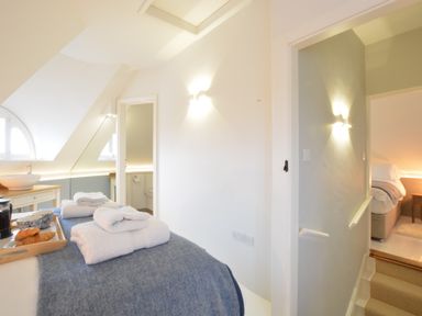 A bedroom with a bed, towels on the bed, a tray with croissants and cups, a sink, and a view into a bathroom and another bedroom at The Round House in Easton near Framlingham