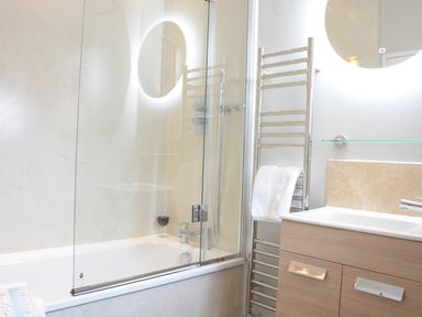 A bathroom with a bathtub shower area a glass shower screen a towel rack with towel and a sink cabinet at The Round House in Easton near Framlingham