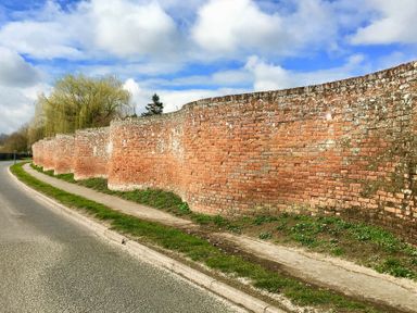 A curved brick wall along a roadside with a sidewalk and grass at The Round House in Easton near Framlingham
