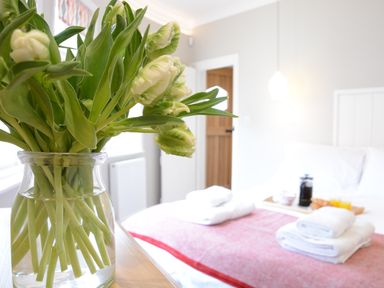 A bedroom with a vase of flowers on a table and a bed with folded towels at The Round House in Easton near Framlingham
