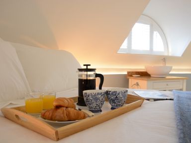A bed with a wooden tray holding croissants orange juice coffee and cups at The Round House in Easton near Framlingham