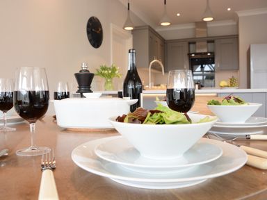 A dining table set with bowls of salad and glasses of red wine in a kitchen at The Round House in Easton near Framlingham