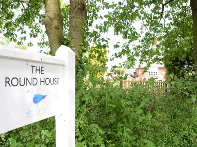 A sign reading The Round House next to trees and bushes with a house and fence in the background at The Round House in Easton near Framlingham