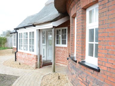 An exterior view of a brick house with white framed windows and a thatched roof at The Round House in Easton near Framlingham