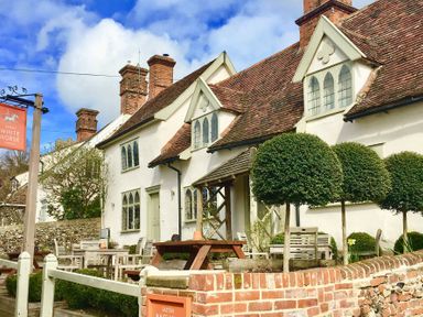 An outdoor seating area with wooden tables and chairs outside a white building with roof windows and brick chimneys at Easton White Horse in Easton near Framlingham