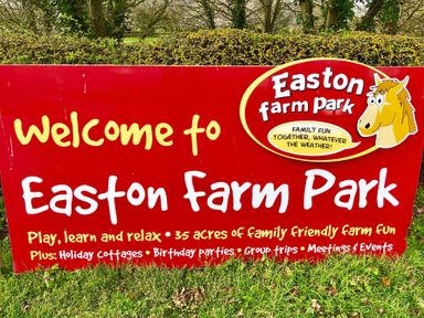 A red welcome sign for Easton Farm Park with information about family activities and facilities on grass with trees in the background at The Round House in Easton near Framlingham