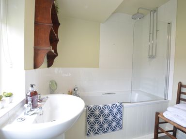 A bathroom with a sink a bathtub with shower and a wooden chair with towels at Church Farm Cottage Dunwich Near Westleton