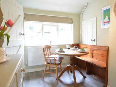 A kitchen dining area with a wooden round table set for four with chairs and a bench by a window at Church Farm Cottage Dunwich Near Westleton