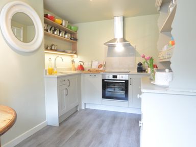 A kitchen with white cabinets an oven a round mirror and shelves with kitchenware at Church Farm Cottage Dunwich Near Westleton