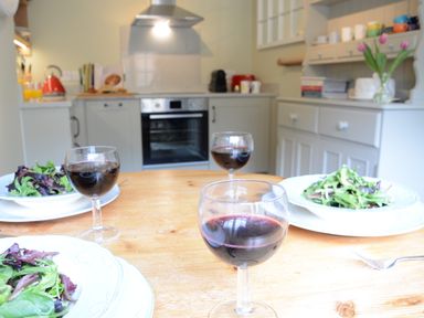 A kitchen with a wooden table set with salad plates and glasses of red wine at Church Farm Cottage Dunwich Near Westleton