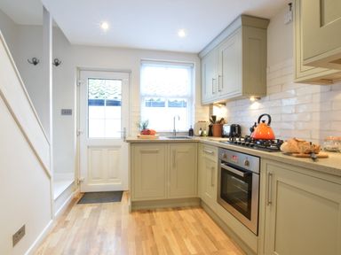 A kitchen with wooden floor cabinets a gas stove oven a sink a white door and a window at 53 Tern Cottage Aldeburgh