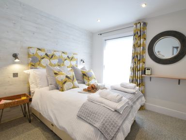 A bedroom with a bed with decorative pillows bedside table and a round mirror on the wall at 53 Tern Cottage Aldeburgh
