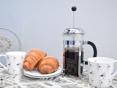 A table with a French press coffee maker two croissants on a plate and two mugs with bird designs at 53 Tern Cottage Aldeburgh