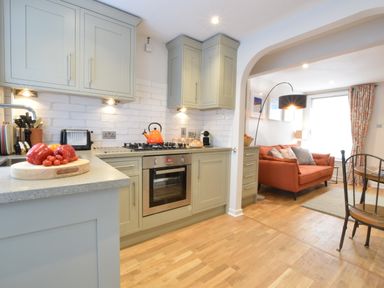 A kitchen with green cabinets and a stove next to a living area with an orange sofa and a floor lamp at 53 Tern Cottage Aldeburgh