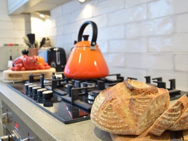 A kitchen countertop with a sliced loaf of bread on a wooden board and an orange kettle on a gas stove at 53 Tern Cottage Aldeburgh