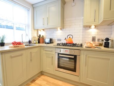 A kitchen with a built-in oven and stove with an orange kettle on it and cabinets at 53 Tern Cottage Aldeburgh