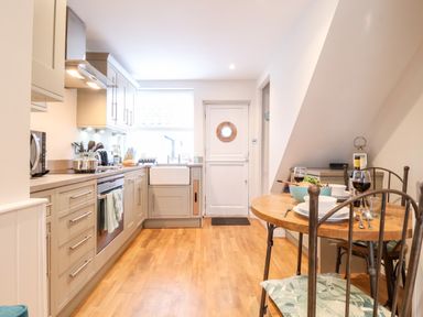 A kitchen with cabinets, oven, microwave, sink, and a dining table with chairs and tableware at 51 Tern Cottage, Aldeburgh