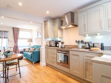 A kitchen with gray cabinets and appliances next to a dining table and a living area with a blue sofa at 51 Tern Cottage Aldeburgh