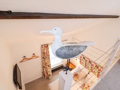 A bedroom with a bed cushions curtains a wall-mounted tv and a large bird decoration at 51 Tern Cottage Aldeburgh