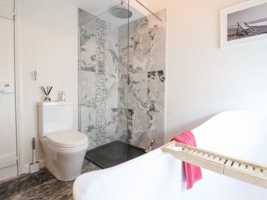 A bathroom with a white toilet, glass shower enclosure, bathtub with wooden tray and pink towel at 51 Tern Cottage Aldeburgh