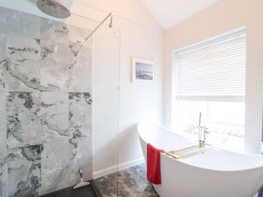 A bathroom with a marble tiled shower area and a freestanding bathtub with a red towel at 51 Tern Cottage Aldeburgh