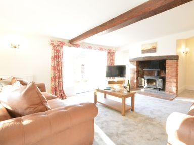 A living room with leather sofas a wooden coffee table a television a brick fireplace and floral curtains at Bedingfield House nr Debenham Debenham