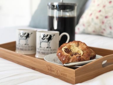A wooden tray with two mugs, a French press coffee maker, and a plate with a pastry and a knife on a bed at Bedingfield House, nr Debenham in Debenham