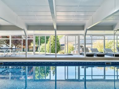 An indoor swimming pool with lounge chairs and a ping pong table behind glass windows at Bedingfield House nr Debenham Debenham